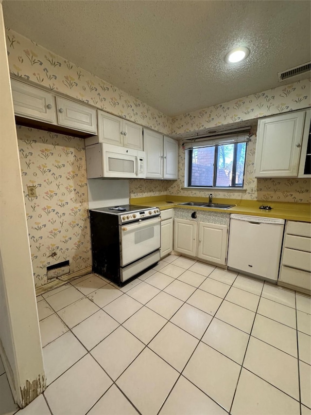 kitchen with a textured ceiling, white appliances, sink, white cabinets, and light tile patterned flooring