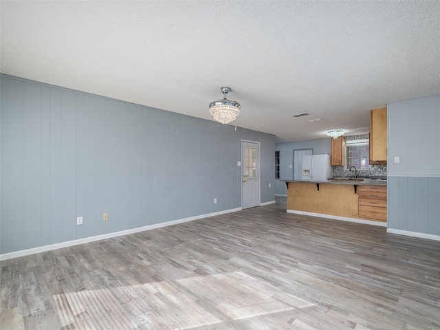 unfurnished living room featuring light hardwood / wood-style floors, sink, a textured ceiling, and a chandelier