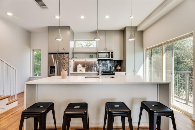 kitchen featuring sink, pendant lighting, decorative backsplash, appliances with stainless steel finishes, and light wood-type flooring