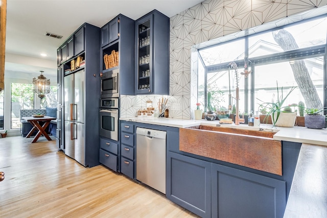 kitchen with appliances with stainless steel finishes, sink, blue cabinetry, pendant lighting, and light hardwood / wood-style floors