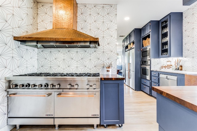 kitchen with blue cabinetry, wood counters, backsplash, built in appliances, and custom exhaust hood