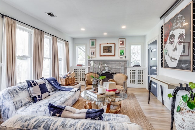 living room featuring light hardwood / wood-style flooring, a stone fireplace, and plenty of natural light