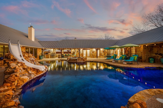 pool at dusk featuring a patio area and a water slide