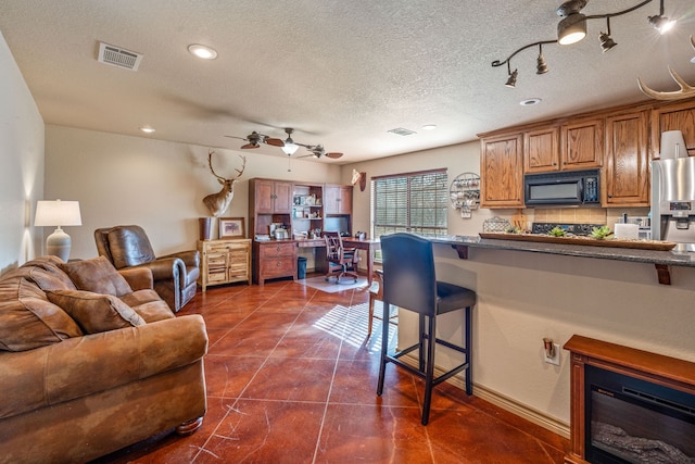 kitchen featuring ceiling fan, a textured ceiling, a kitchen bar, decorative backsplash, and dark tile patterned flooring