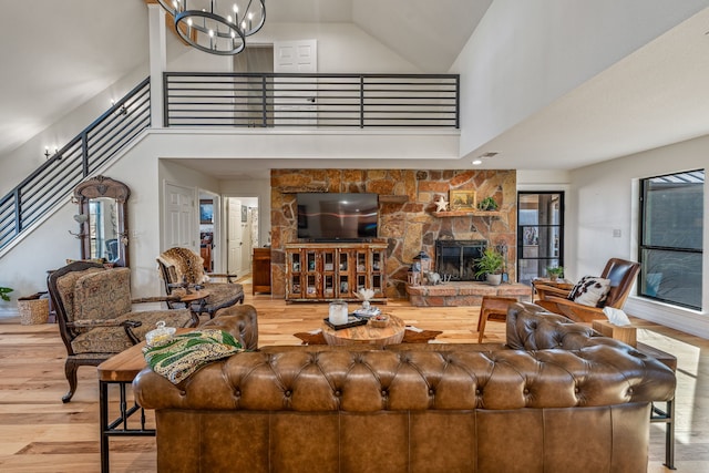 living room with a chandelier, a fireplace, a high ceiling, and light hardwood / wood-style flooring