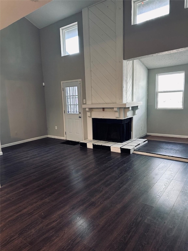 unfurnished living room with a fireplace, a towering ceiling, plenty of natural light, and dark wood-type flooring