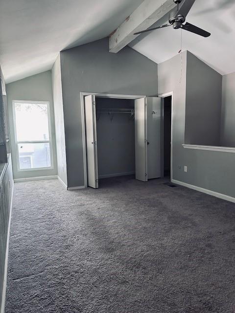 unfurnished bedroom with ceiling fan, lofted ceiling with beams, and dark colored carpet