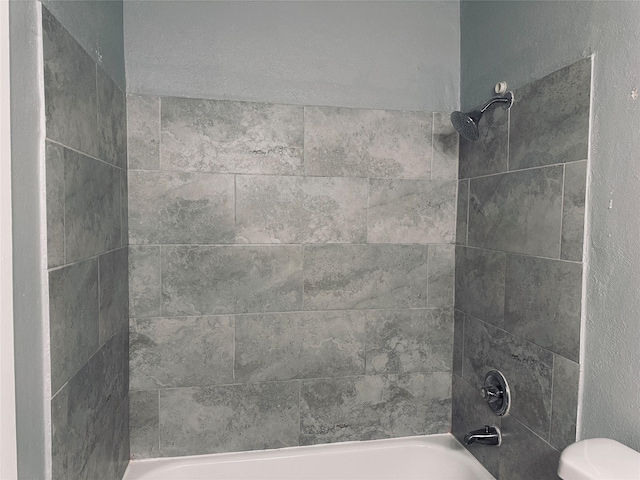 bathroom featuring tiled shower / bath combo and toilet