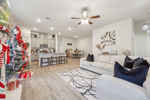 living room featuring ceiling fan, sink, and light hardwood / wood-style floors