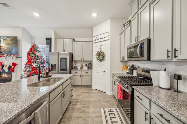 kitchen featuring decorative backsplash, light wood-type flooring, light stone counters, stainless steel appliances, and sink