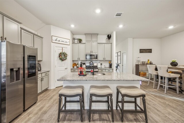 kitchen with a kitchen breakfast bar, a kitchen island with sink, light stone counters, and appliances with stainless steel finishes