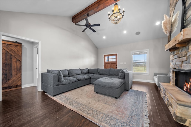 living room featuring a stone fireplace, a barn door, dark hardwood / wood-style flooring, lofted ceiling with beams, and ceiling fan with notable chandelier