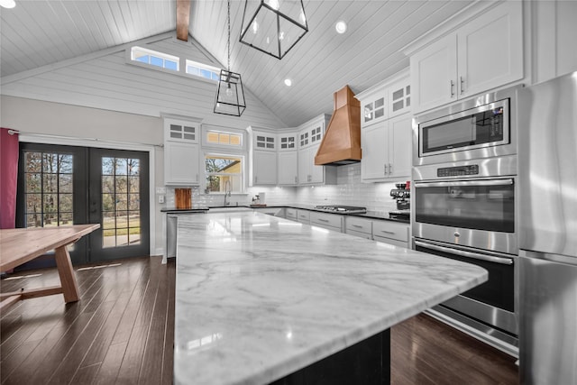 kitchen with premium range hood, dark stone counters, beamed ceiling, decorative light fixtures, and white cabinetry