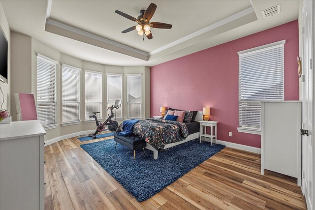 bedroom featuring hardwood / wood-style floors, ceiling fan, a raised ceiling, and ornamental molding