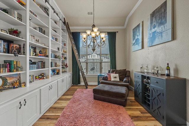 living area featuring a chandelier, a barn door, light hardwood / wood-style flooring, and ornamental molding