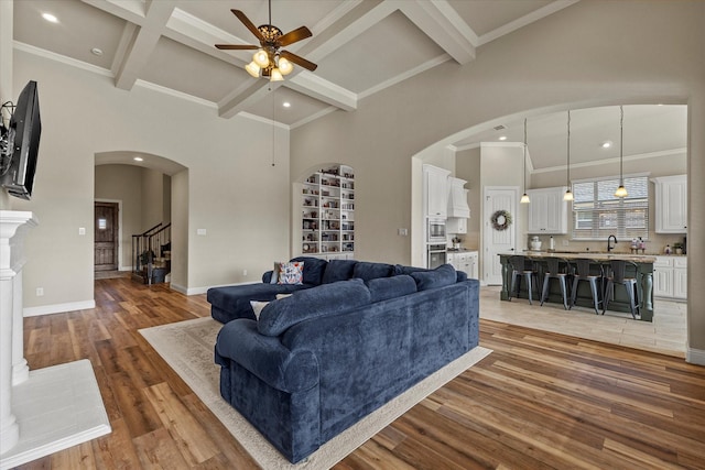 living room with a high ceiling, sink, ceiling fan, beamed ceiling, and wood-type flooring