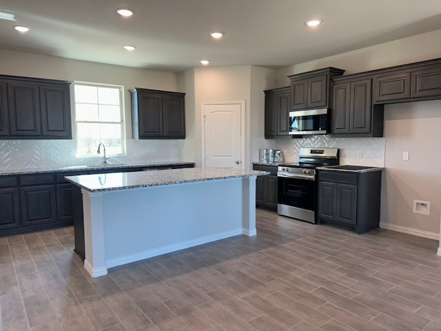 kitchen featuring stainless steel appliances, light wood-style flooring, light stone countertops, and a center island