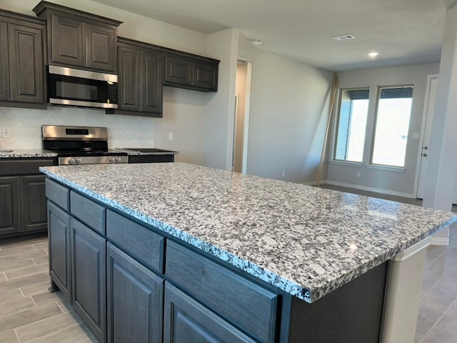 kitchen featuring stainless steel appliances, a kitchen island, backsplash, and light stone counters