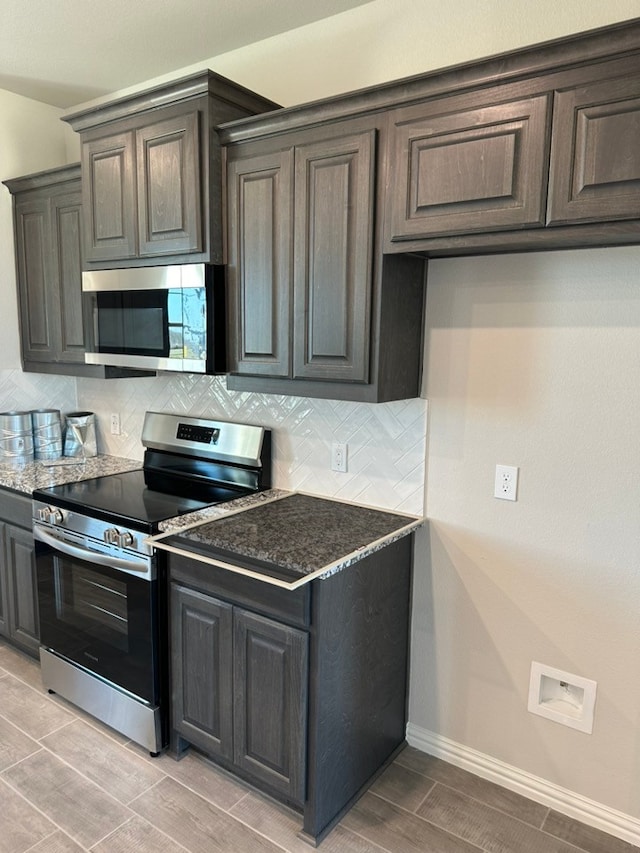 kitchen with wood finish floors, backsplash, appliances with stainless steel finishes, dark stone countertops, and baseboards