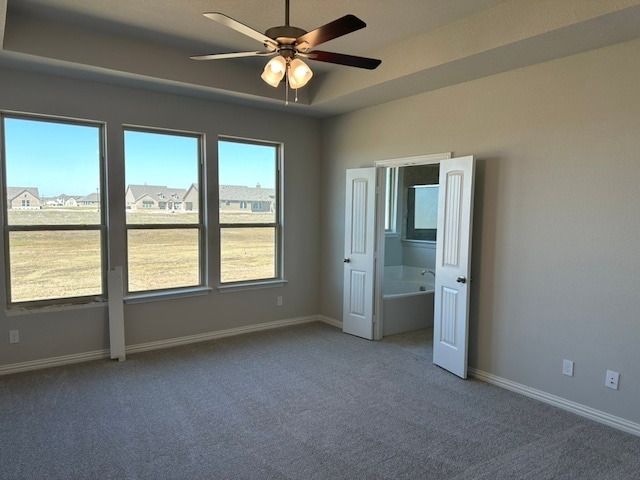 unfurnished room featuring a tray ceiling, carpet flooring, a ceiling fan, and baseboards