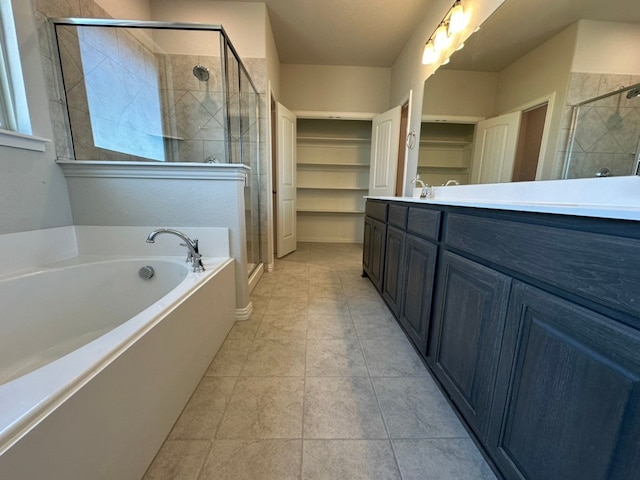 full bathroom featuring a walk in closet, a stall shower, vanity, a bath, and tile patterned floors