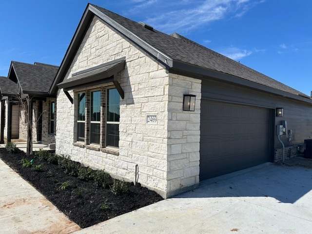 view of side of home featuring stone siding, a shingled roof, an attached garage, and cooling unit