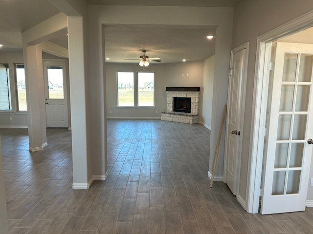 unfurnished living room featuring a ceiling fan, baseboards, dark wood-type flooring, and a stone fireplace