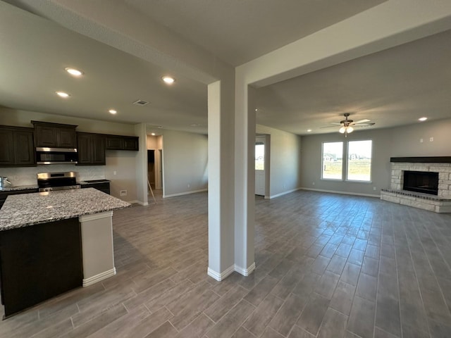 kitchen with a fireplace with raised hearth, stainless steel appliances, open floor plan, and wood finished floors