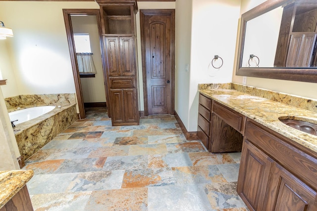 bathroom with stone finish floor, a garden tub, vanity, and baseboards