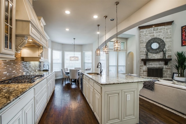 kitchen with sink, a stone fireplace, decorative light fixtures, a center island with sink, and appliances with stainless steel finishes