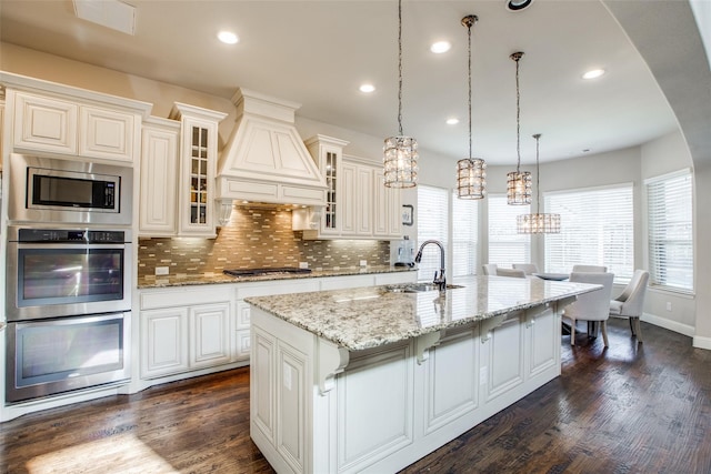 kitchen with sink, premium range hood, decorative backsplash, a center island with sink, and appliances with stainless steel finishes