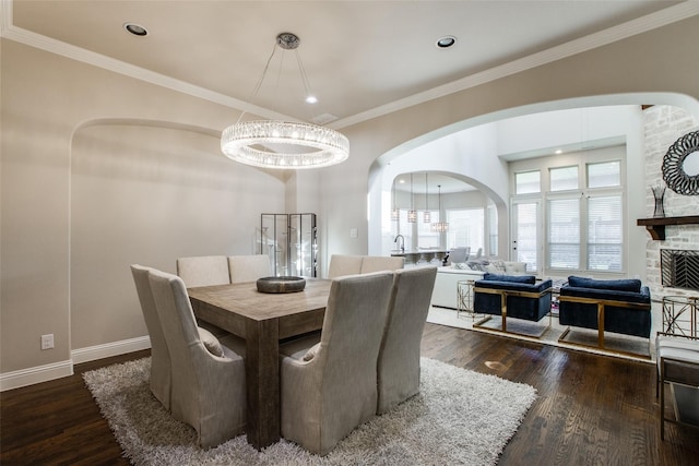 dining room featuring a stone fireplace, dark hardwood / wood-style flooring, crown molding, and an inviting chandelier