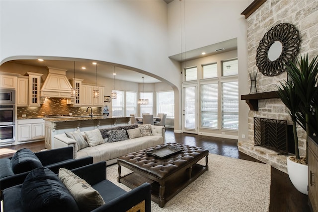 living room with a stone fireplace, a towering ceiling, and dark wood-type flooring