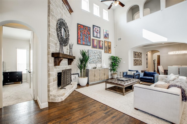 living room with hardwood / wood-style flooring, ceiling fan, a stone fireplace, and a high ceiling