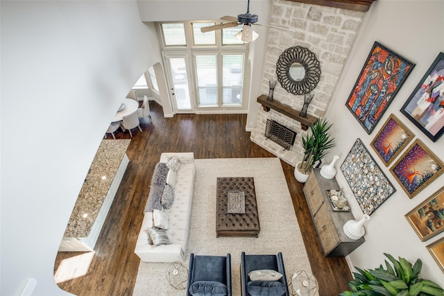 living room with dark hardwood / wood-style flooring, ceiling fan, a stone fireplace, and a high ceiling