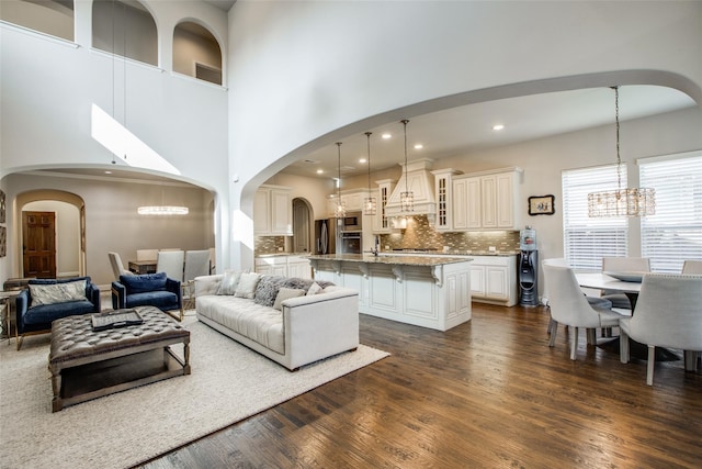 living room featuring a towering ceiling, dark wood-type flooring, and a notable chandelier