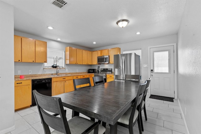 kitchen with sink, light tile patterned floors, a textured ceiling, light brown cabinetry, and appliances with stainless steel finishes