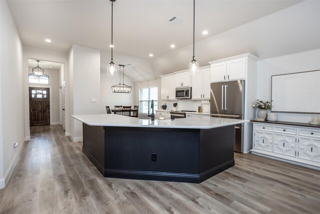 kitchen with stainless steel appliances, vaulted ceiling, decorative light fixtures, white cabinetry, and a large island