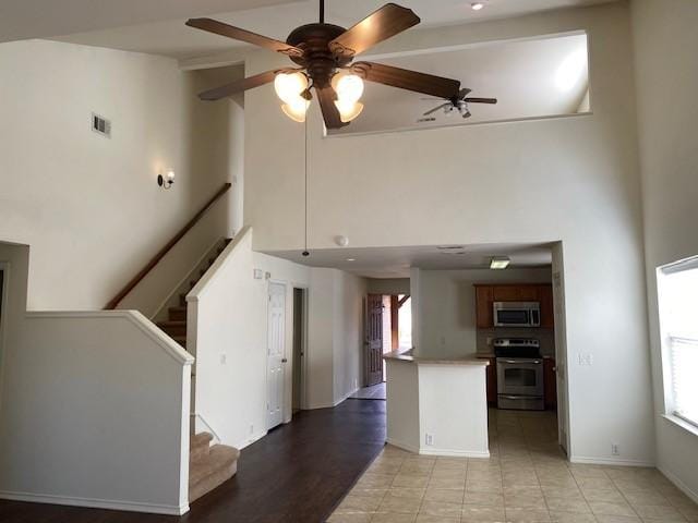 kitchen with kitchen peninsula, ceiling fan, stove, and a high ceiling