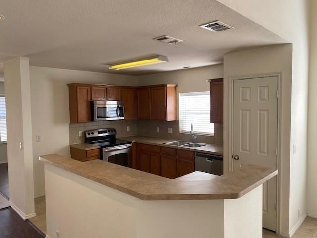 kitchen with sink, a center island, backsplash, kitchen peninsula, and appliances with stainless steel finishes