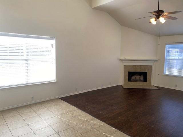 unfurnished living room with ceiling fan, a fireplace, light tile patterned floors, and vaulted ceiling