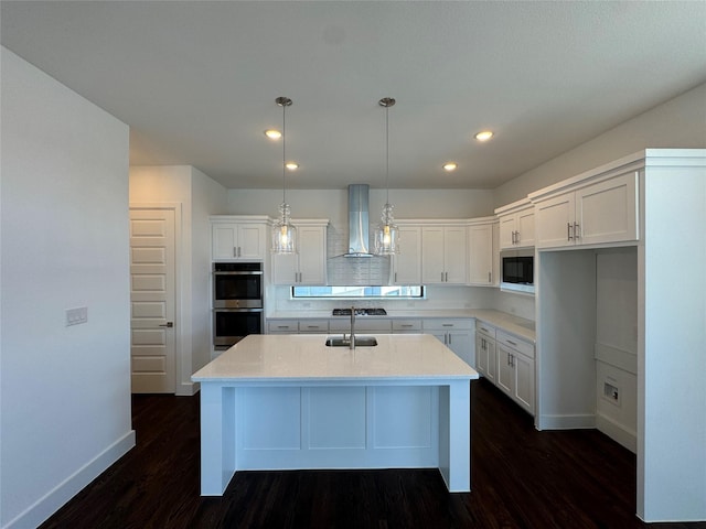 kitchen with white cabinets, wall chimney range hood, stainless steel appliances, and an island with sink