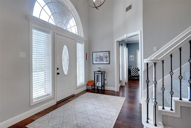 entryway featuring a towering ceiling, dark wood-type flooring, and a notable chandelier