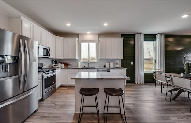 kitchen featuring light stone countertops, appliances with stainless steel finishes, sink, white cabinets, and a kitchen island