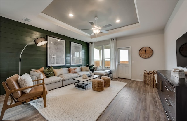 living room featuring light hardwood / wood-style flooring, a raised ceiling, ceiling fan, and wood walls