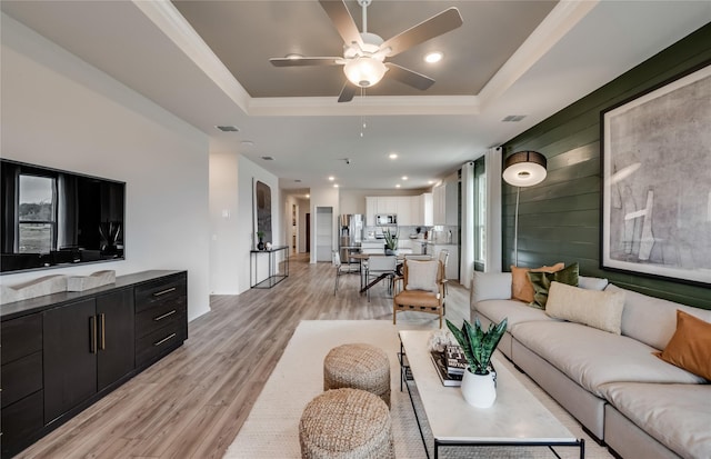 living room with a tray ceiling, wooden walls, ceiling fan, and light wood-type flooring