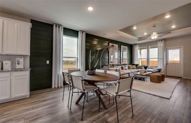 dining space with ceiling fan, a raised ceiling, and light wood-type flooring