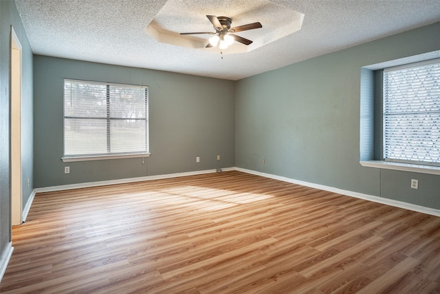 empty room with a tray ceiling, plenty of natural light, ceiling fan, and light hardwood / wood-style floors