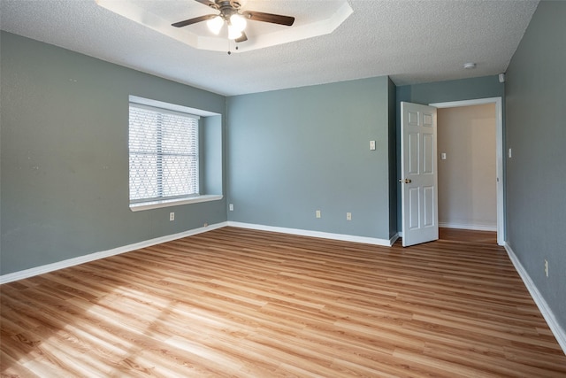 unfurnished room with a textured ceiling, light wood-type flooring, a tray ceiling, and ceiling fan