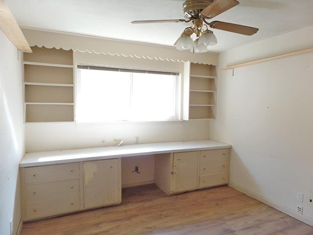 unfurnished office featuring ceiling fan, light wood-type flooring, and built in desk